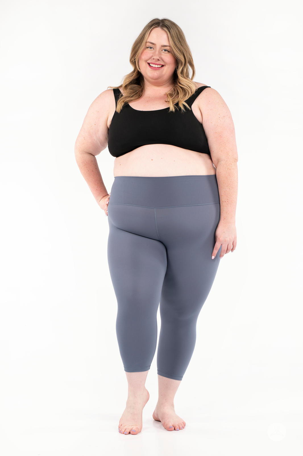 Plus-size woman smiling wearing gray Free Motion Crops by Athleisure SweetLegs collection standing barefoot on white background