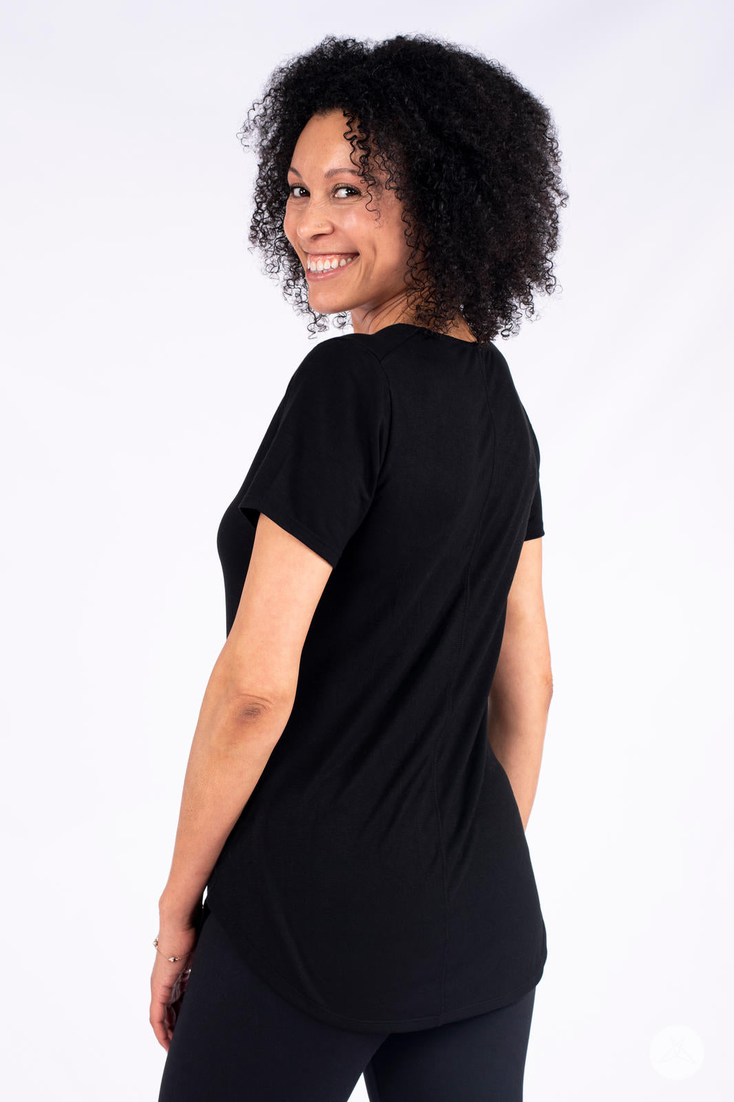 Smiling woman wearing black Classic Tee by SweetLegs Canada with short sleeves and curved high-low hem back view