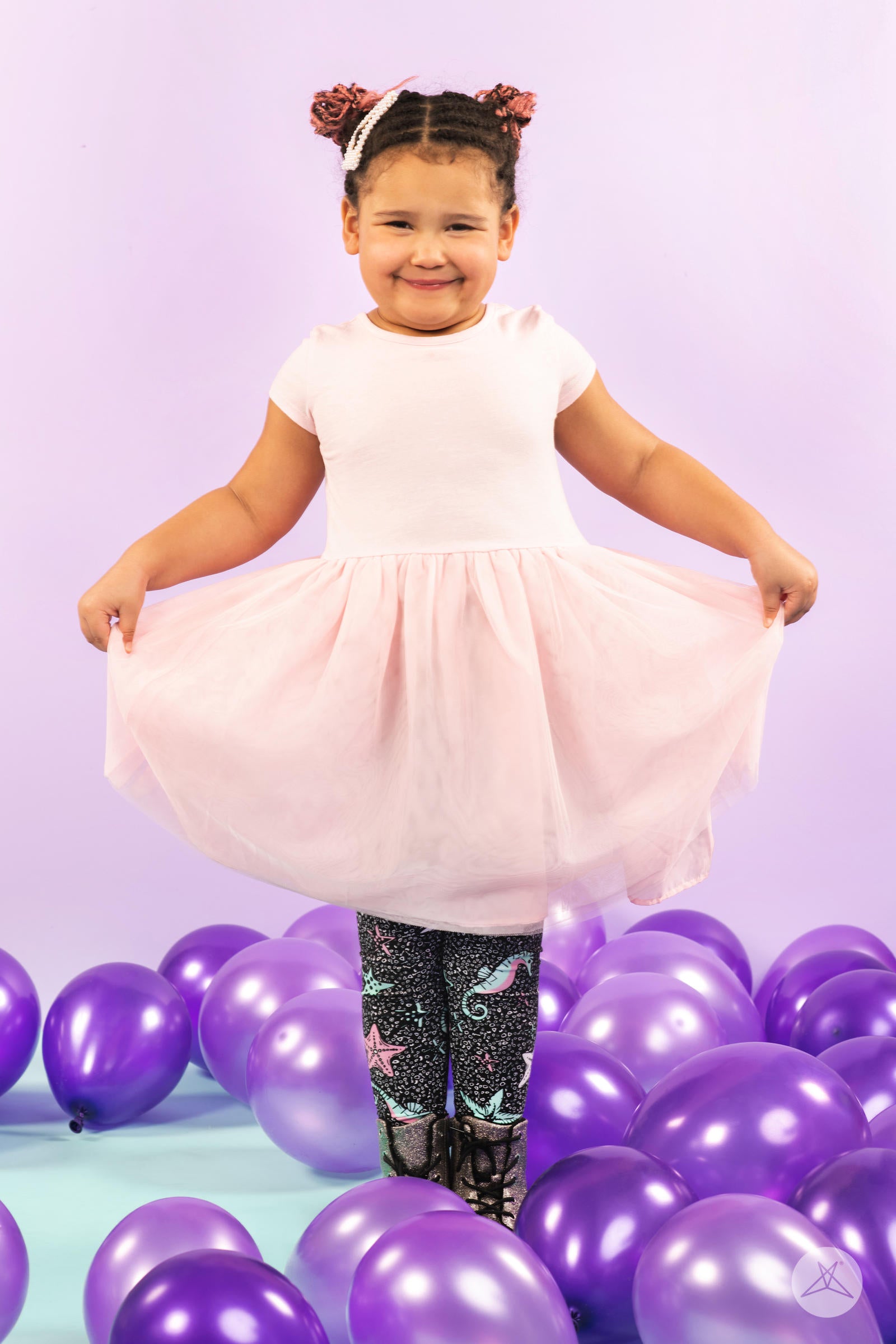 Smiling child wearing SweetLegs Under The Sea Kids leggings with sea creature patterns among purple balloons