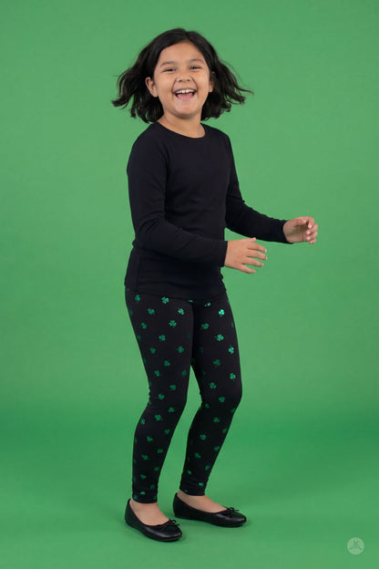 Happy child wearing Lucky Glow Kids leggings with emerald shamrock print by SweetLegs on green background