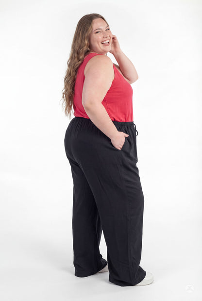 Plus size woman smiling wearing black Breeze Wide-Leg Pant by sweetlegs with hands in pockets standing against white background