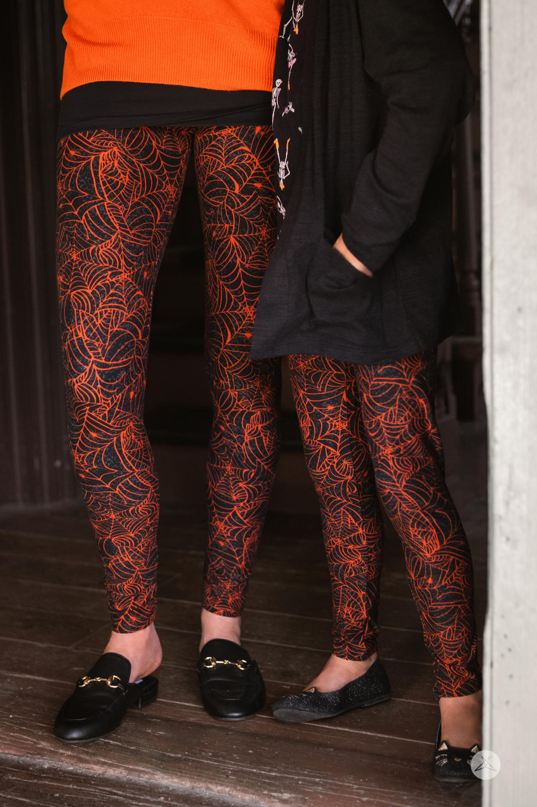 SweetLegs Spells & Threads Kids leggings with vibrant orange spider web design on black fabric worn by child and adult model