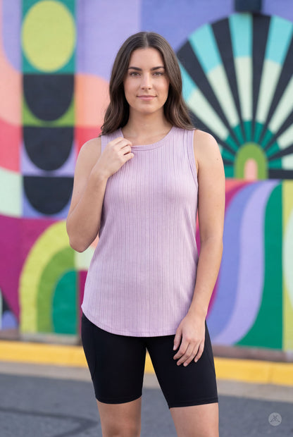 Woman wearing SweetTops The Soft Ribbed Tank in lilac with black shorts, standing against a colorful mural background