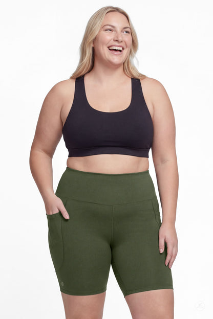 Smiling plus size woman wearing SweetLegs Cedar High-Waisted Pocket Biker Shorts in green with black sports bra front view