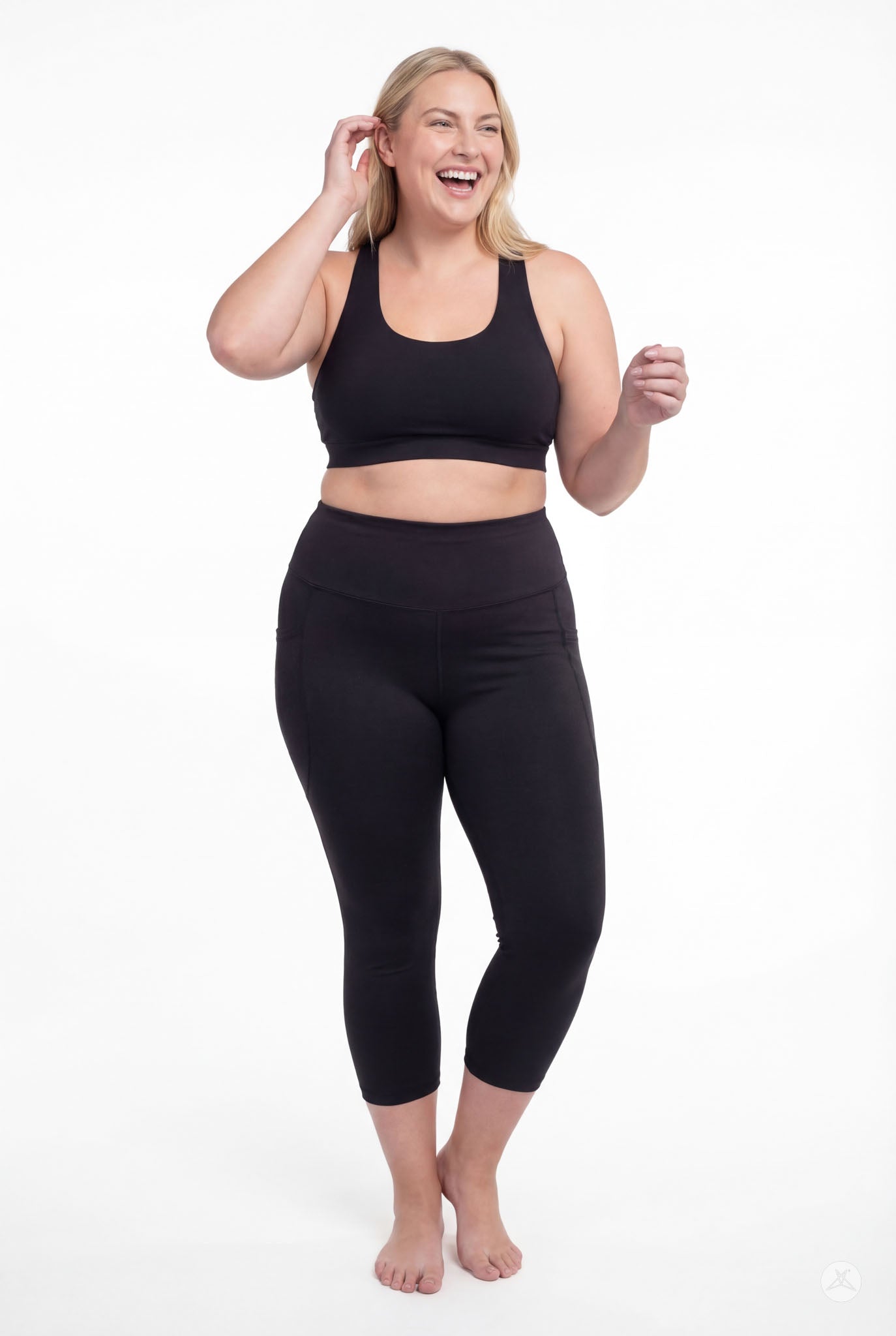 Smiling woman barefoot wearing SweetLegs Black High-Waisted Pocket Crops with black sports bra in relaxed pose