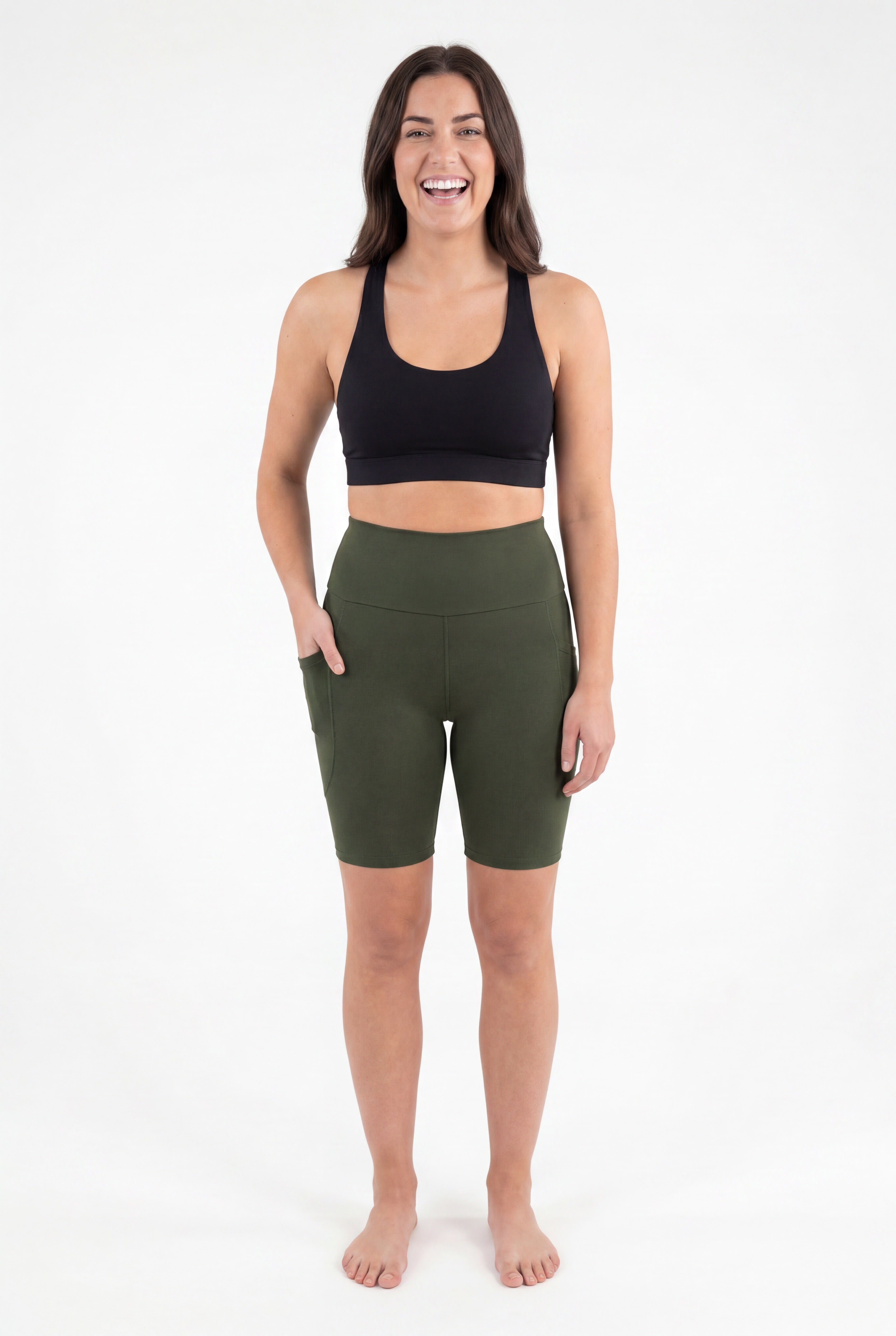 Smiling woman wearing SweetLegs Cedar High-Waisted Pocket Biker Shorts in green with black sports bra front view barefoot