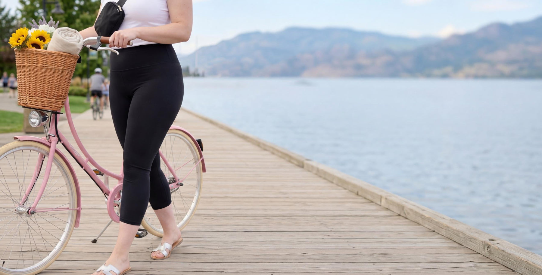 Woman walking with a pink bicycle by a lake with mountains in the background