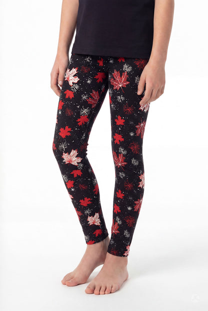 Child wearing SweetLegs Maple Mood Kids leggings with red and white maple leaf pattern on black background barefoot