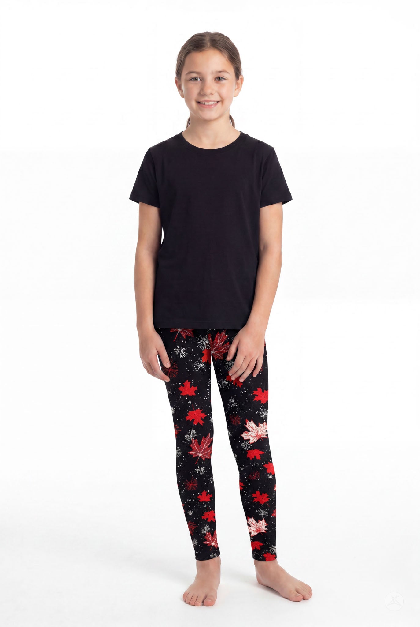Girl wearing SweetLegs Maple Mood Kids leggings with red and white maple leaf pattern paired with black shirt barefoot