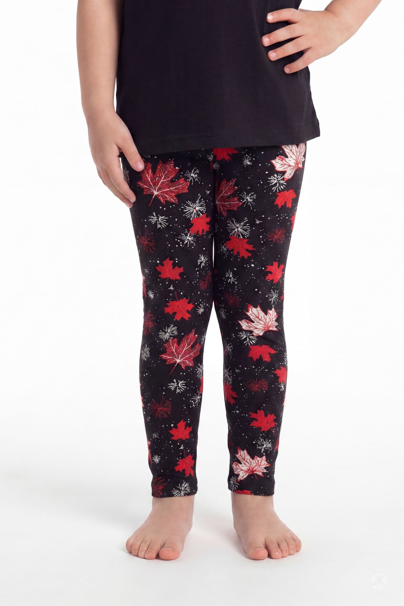 Child wearing SweetLegs Maple Mood Kids leggings with red and white maple leaf pattern and black top barefoot