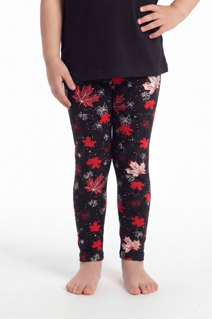 Child wearing SweetLegs Maple Mood Kids leggings with red and white maple leaf pattern and black top barefoot