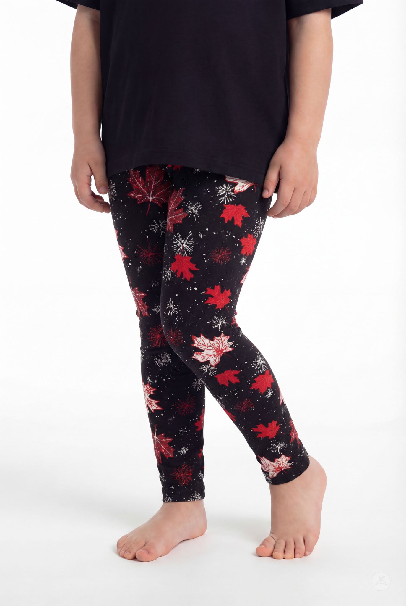 Child wearing SweetLegs Maple Mood Kids leggings with red and white maple leaves on black background barefoot