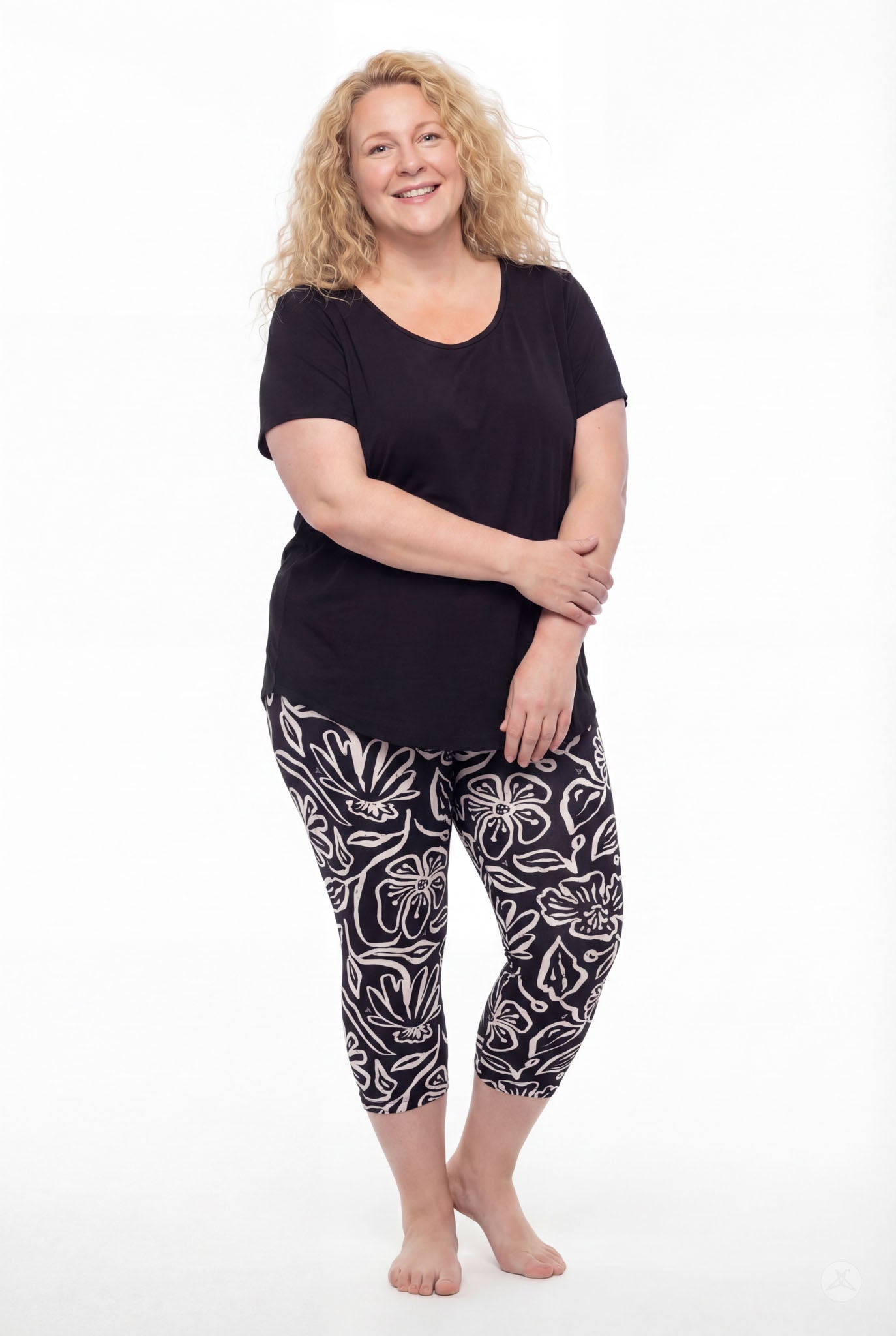 Plus size model in SweetLegs Midnight Bloom Crops with black and white floral pattern paired with black top barefoot smiling