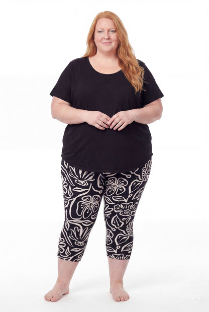 Plus size woman in SweetLegs Midnight Bloom Crops with bold beige floral pattern paired with black top barefoot standing front view