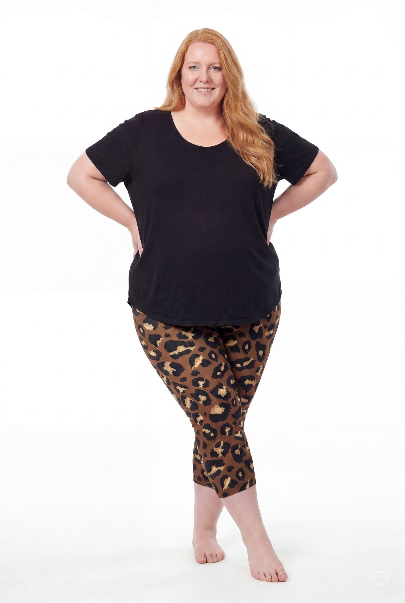 Smiling woman wearing SweetLegs Mocha Spots Crops with bold brown leopard spots and a black tee barefoot standing