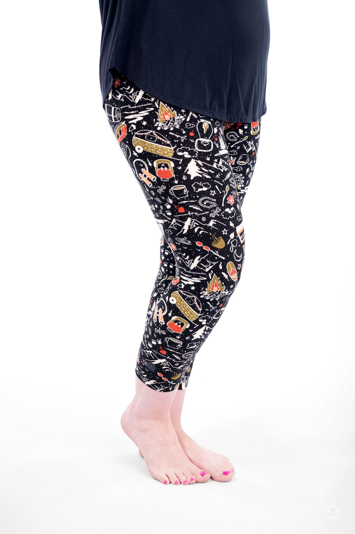Person wearing SweetLegs Off Grid Crops with camping-themed pattern and black top standing barefoot side view