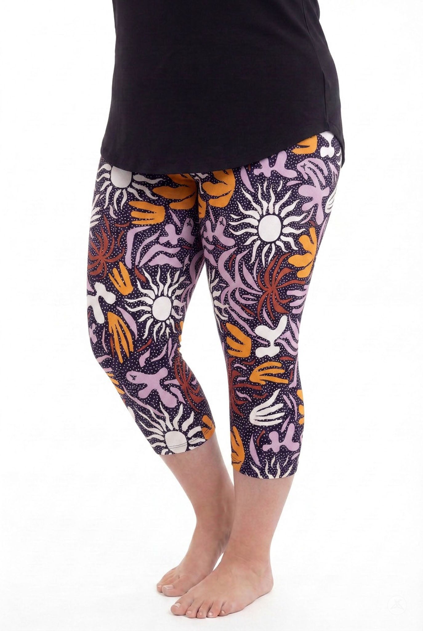 Woman barefoot wearing SweetLegs Retro Petals Crops featuring colorful abstract floral and sun patterns with a black top