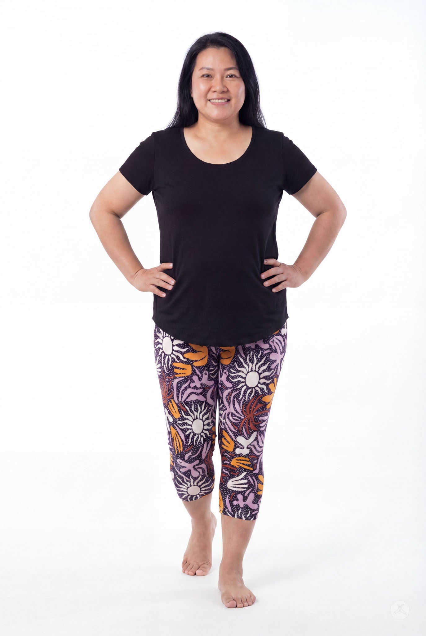 Woman smiling wearing SweetLegs Retro Petals Crops with purple, orange, and white floral patterns and black tee barefoot
