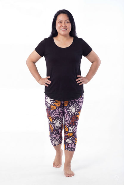 Woman smiling wearing SweetLegs Retro Petals Crops with purple, orange, and white floral patterns and black tee barefoot