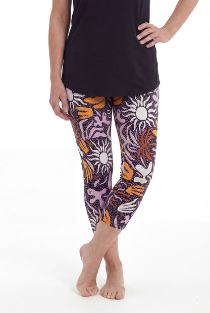 Woman barefoot wearing SweetLegs Retro Petals Crops with artistic sun and abstract floral patterns in purple, orange, and white