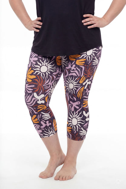 Woman wearing SweetLegs Retro Petals Crops with vibrant orange, purple, and white floral pattern and black top barefoot