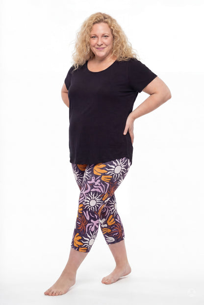 Smiling woman with curly hair wearing SweetLegs Retro Petals Crops in purple, orange, and white floral patterns and black top