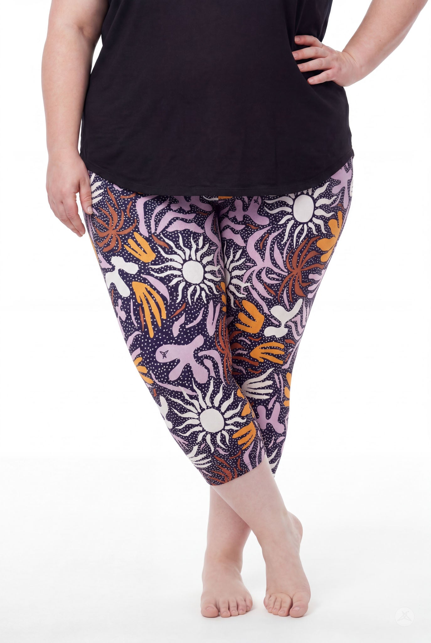 Curvy woman wearing SweetLegs Retro Petals Crops with white sun shapes and orange, purple abstract patterns barefoot