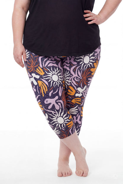 Curvy woman wearing SweetLegs Retro Petals Crops with white sun shapes and orange, purple abstract patterns barefoot