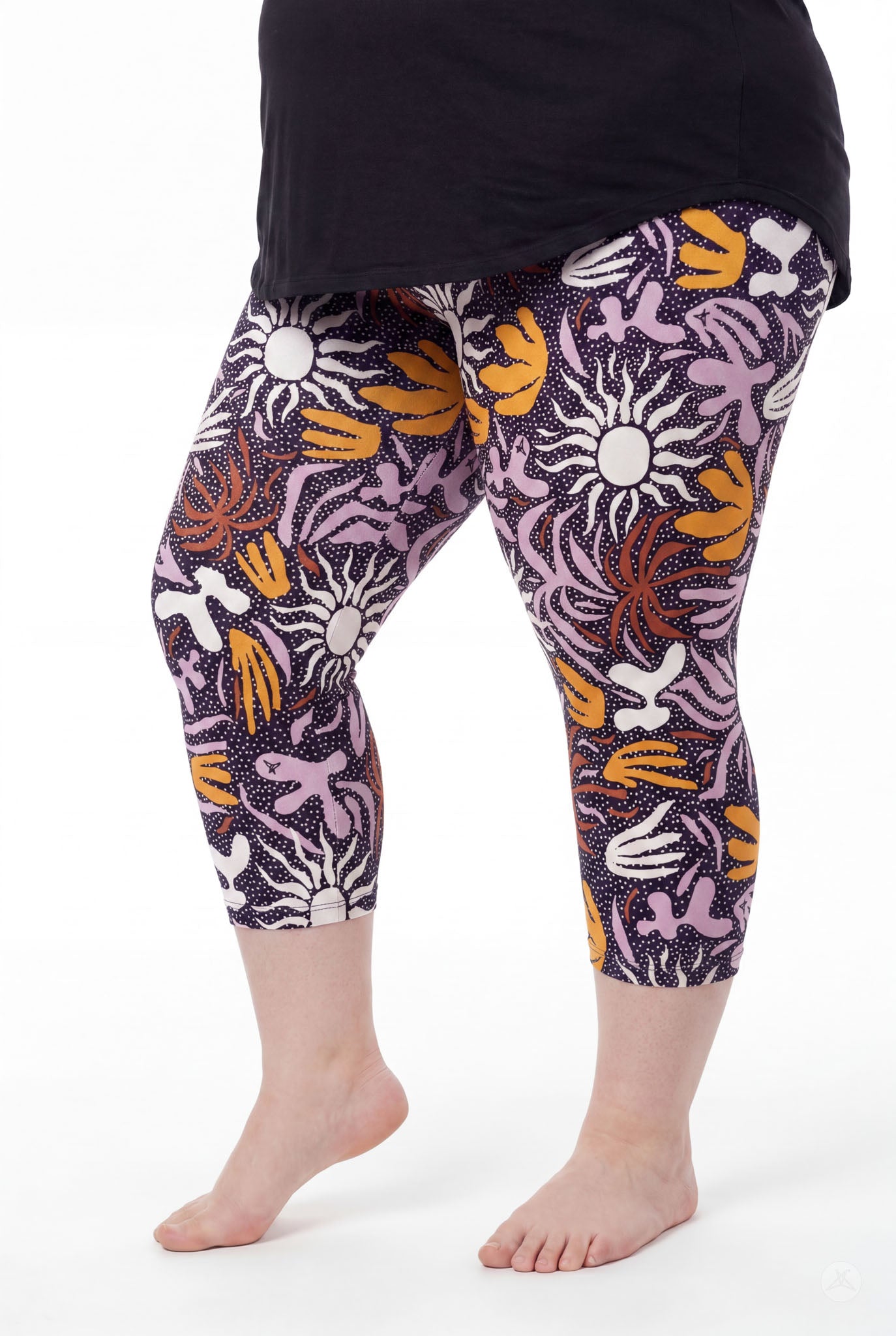 Curvy woman barefoot wearing SweetLegs Retro Petals Crops with bold orange, purple, and white floral and sun patterns