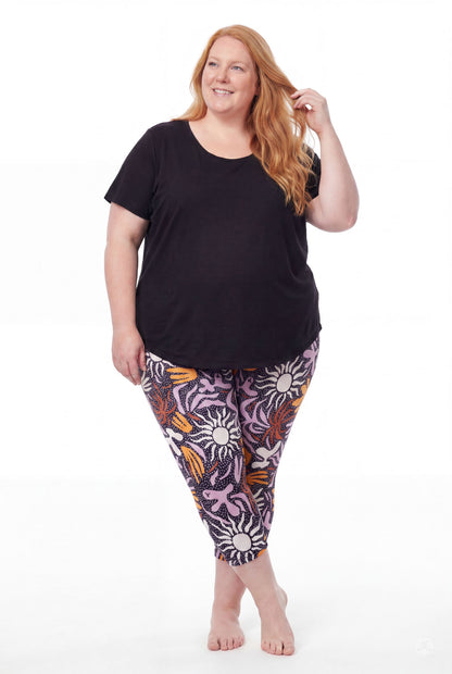Smiling woman wearing SweetLegs Retro Petals Crops with high-waisted colorful sun and floral patterns and black top barefoot