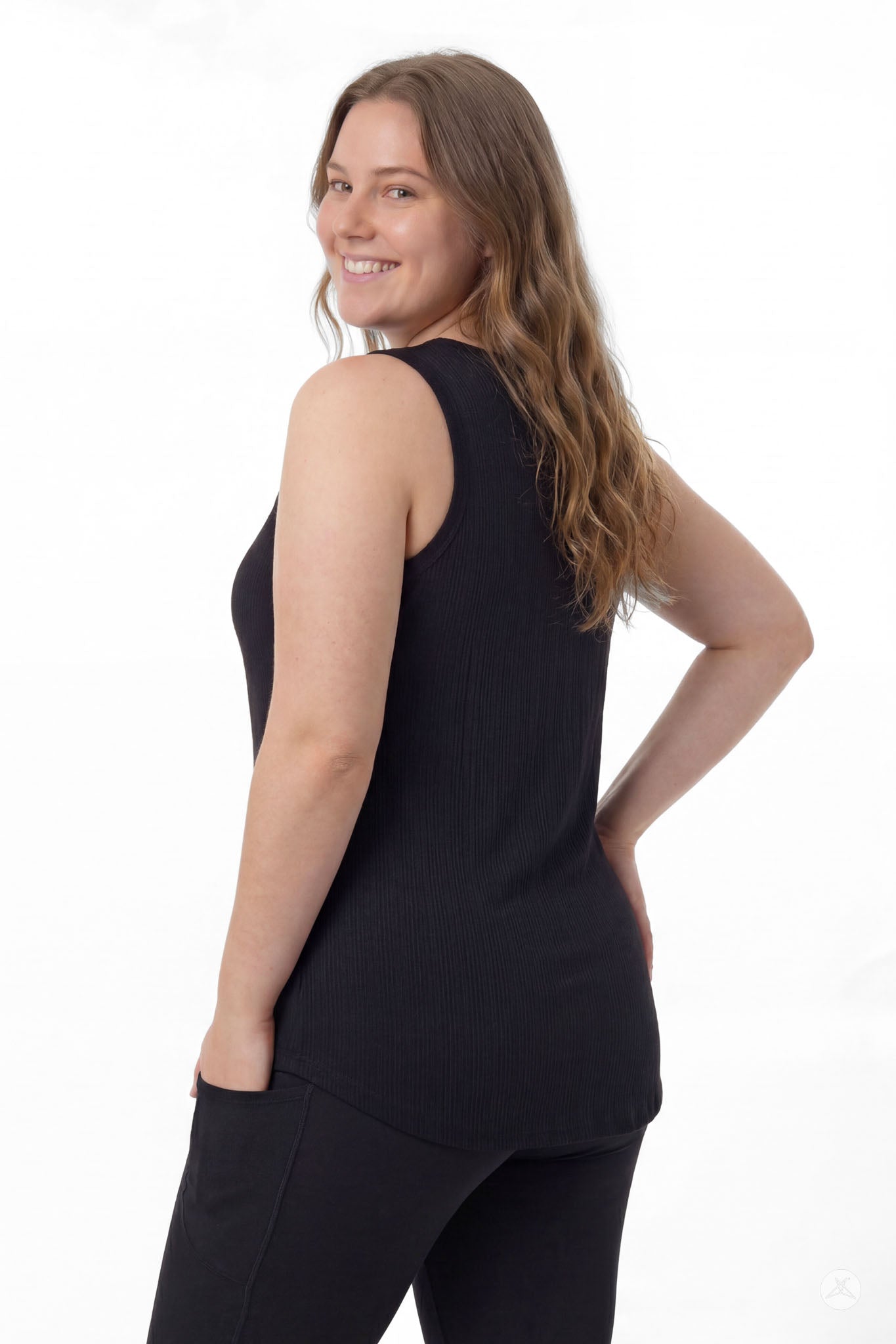 Woman smiling over shoulder wearing SweetTops The Soft Ribbed Tank in black with black pants, back view