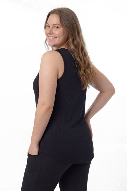 Woman smiling over shoulder wearing SweetTops The Soft Ribbed Tank in black with black pants, back view