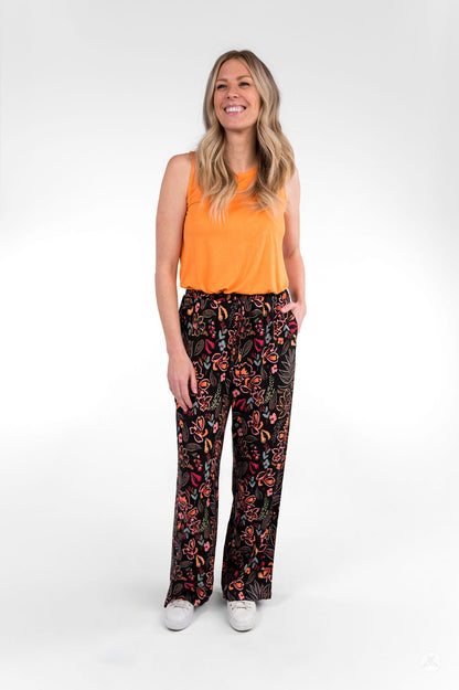Smiling woman wearing sweetlegs Breeze Wide-Leg Pant with colorful floral print paired with orange sleeveless top