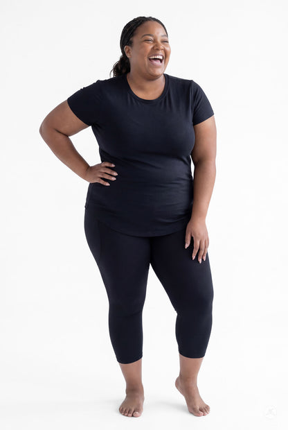 Happy plus size woman barefoot wearing SweetLegs Black Pocket Crops and black short sleeve top standing on white background