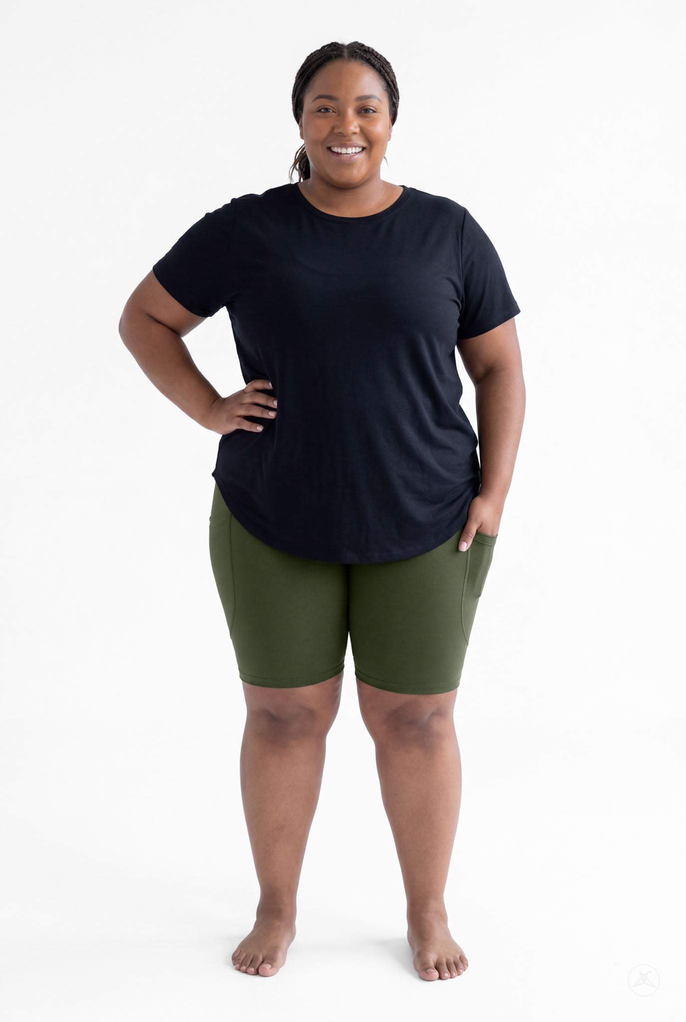 Plus size woman smiling barefoot wearing SweetLegs Cedar Pocket Biker Shorts in green with hand in side pocket standing front view