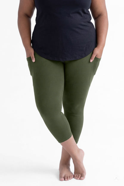 Plus size woman standing barefoot wearing SweetLegs Cedar Pocket Crops in olive green leggings with pockets and black top