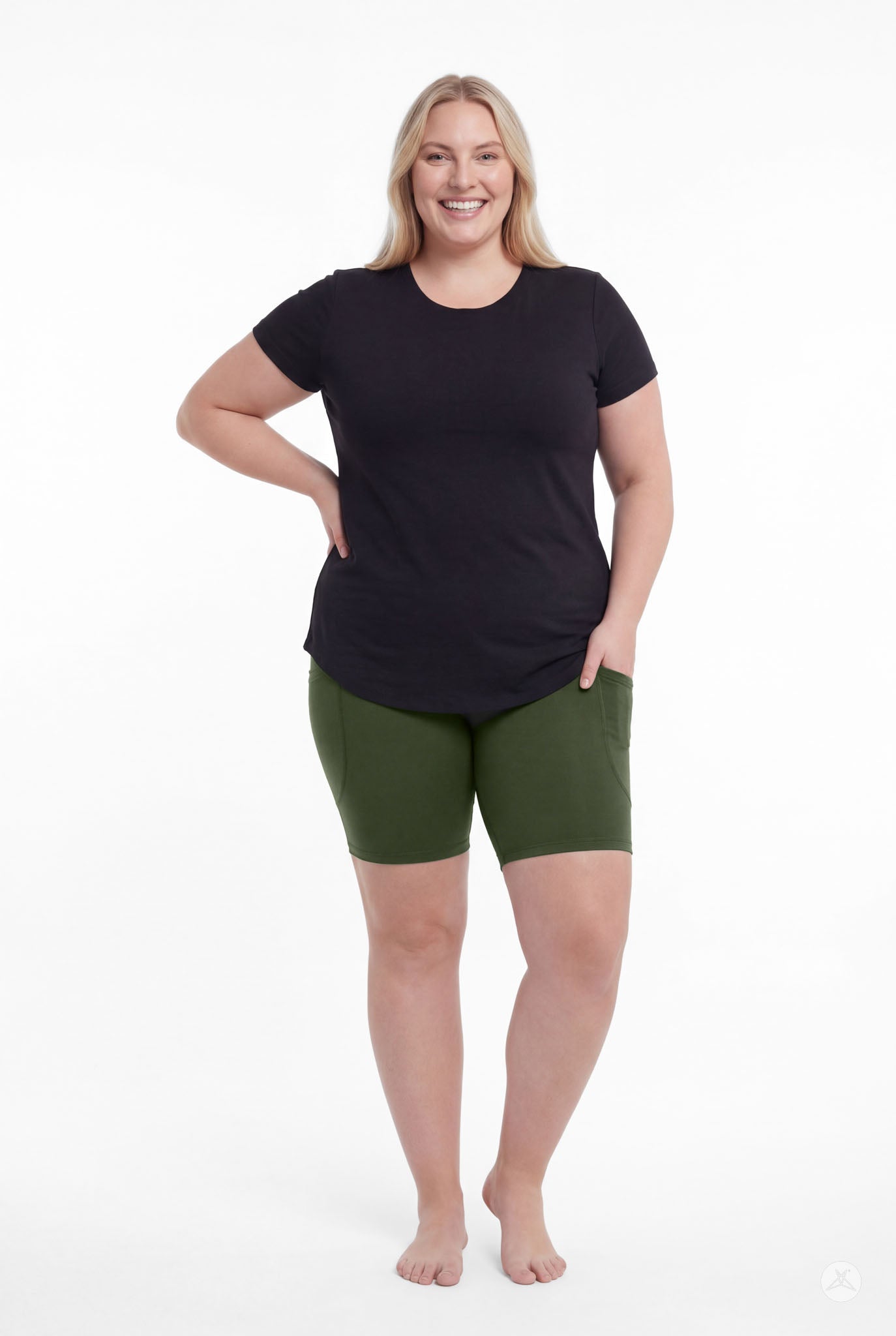 Smiling woman wearing SweetLegs Cedar Pocket Biker Shorts in green with black top standing with hand in pocket front view