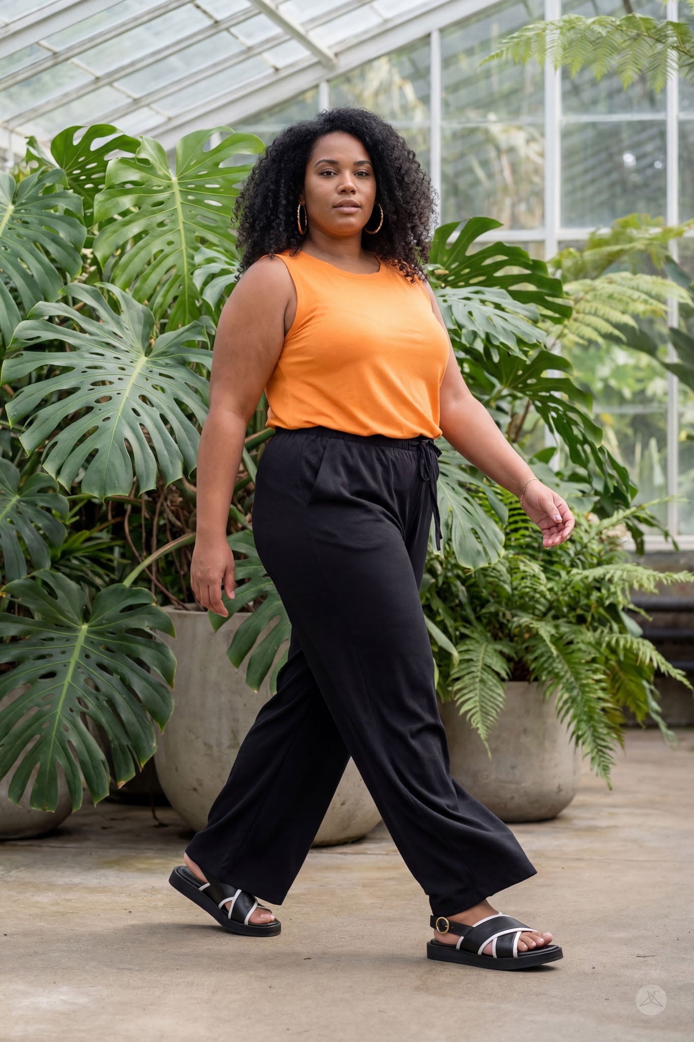 Plus size model walking indoors wearing sweetlegs Breeze Wide-Leg Pant in black and orange sleeveless top