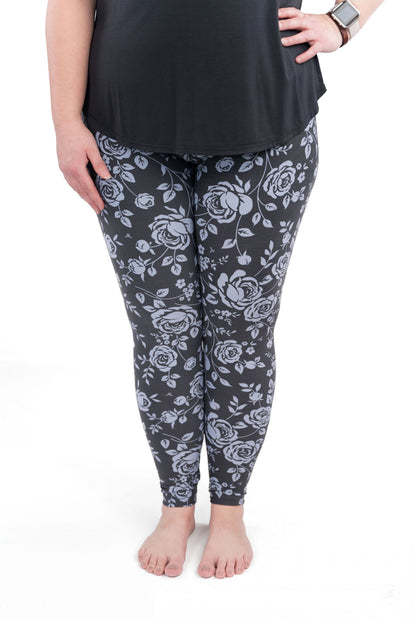 Close-up of legs wearing SweetLegs Shadow Garden leggings with grey-blue floral print on dark background
