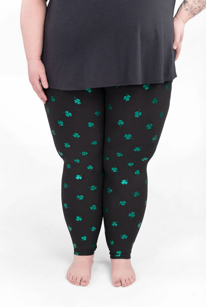 Plus size model wearing SweetLegs Lucky Glow leggings with emerald shamrock print on black background