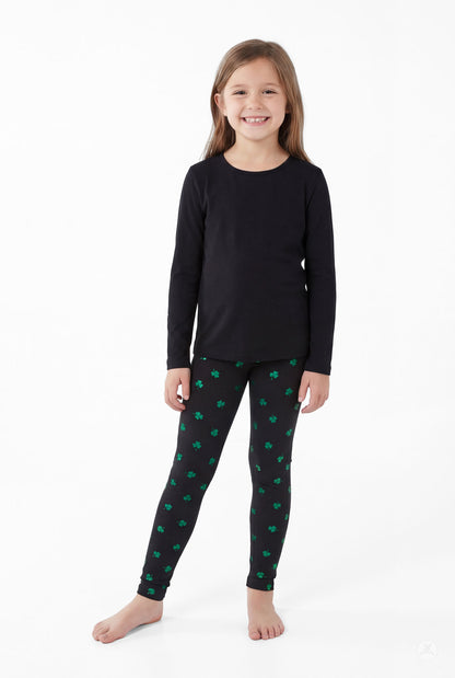 Smiling girl wearing Lucky Glow Kids black leggings with green shamrocks by SweetLegs and a plain black long sleeve top