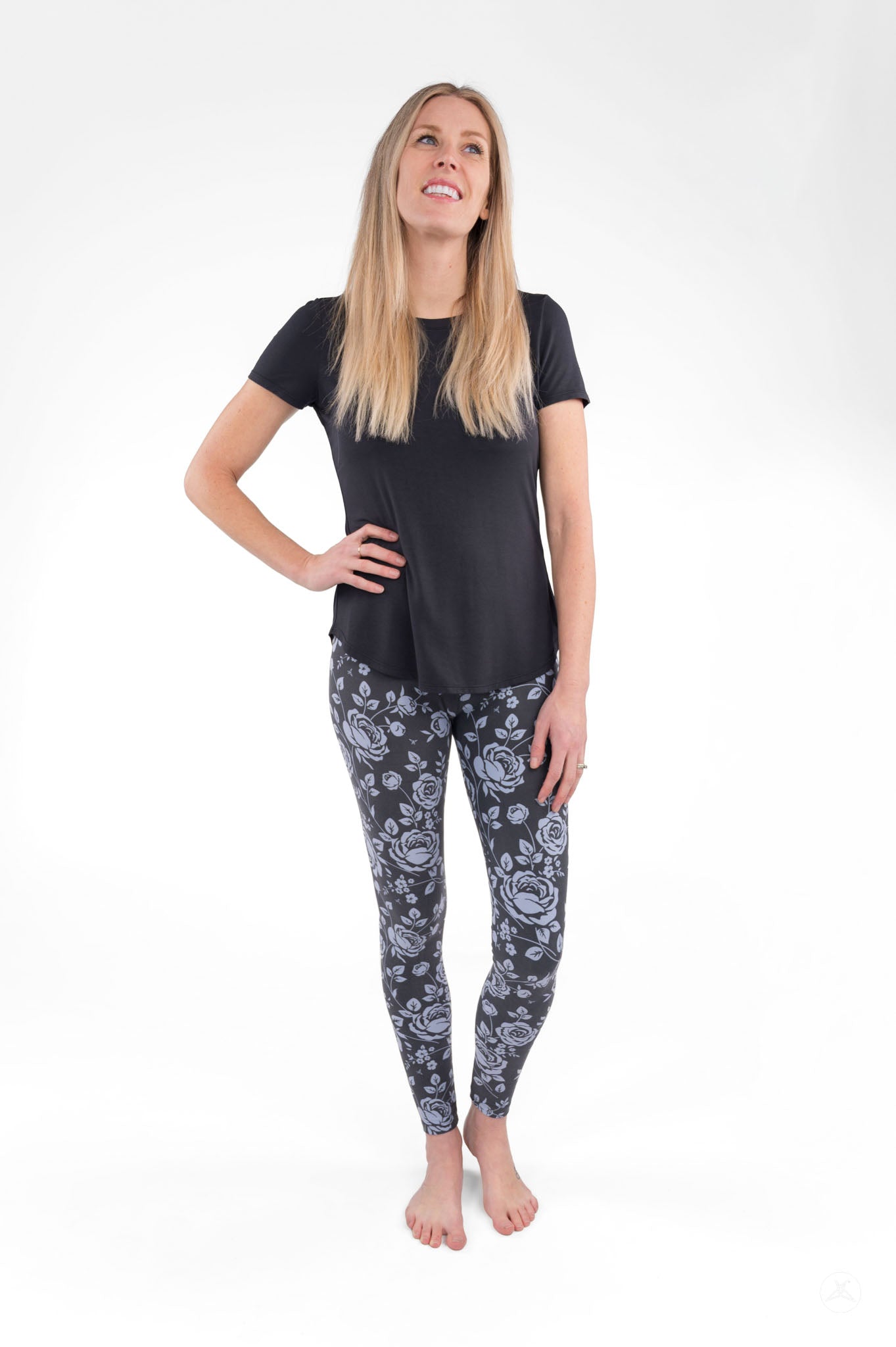 Woman wearing SweetLegs Shadow Garden leggings with grey-blue floral print paired with a black top on white background