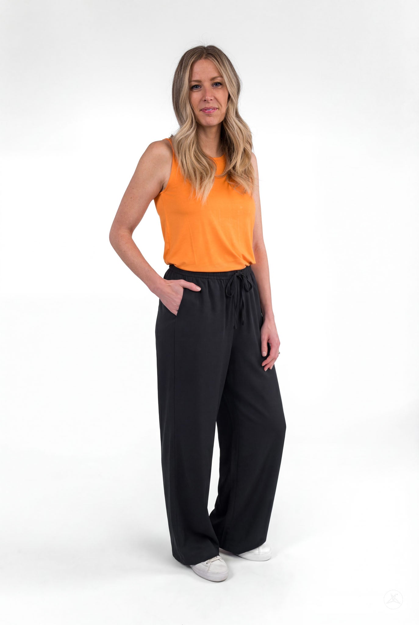 Woman wearing black Breeze Wide-Leg Pant by sweetlegs with orange sleeveless top standing with hands in pockets