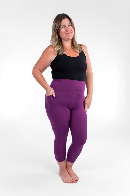 Smiling woman wearing sweetlegs Deep Plum High-Waisted Pocket Crops with black tank top standing barefoot with hands in pockets