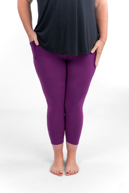 Person standing barefoot wearing sweetlegs Deep Plum Pocket Crops with hands resting lightly on hips and black top