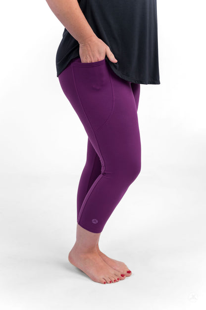 Person barefoot wearing sweetlegs Deep Plum Pocket Crops in vibrant purple with hand in pocket and black top visible from waist down