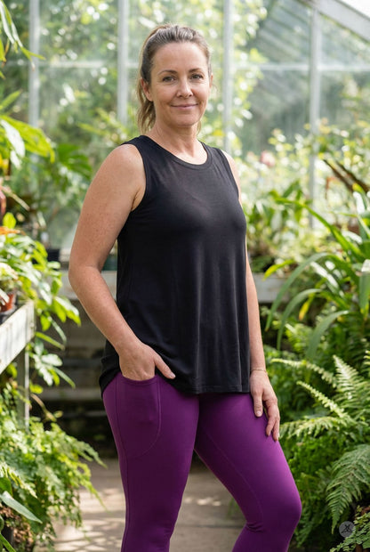 Woman standing in garden wearing sleeveless black High Neck Tank by sweettops and purple leggings with hands in pockets