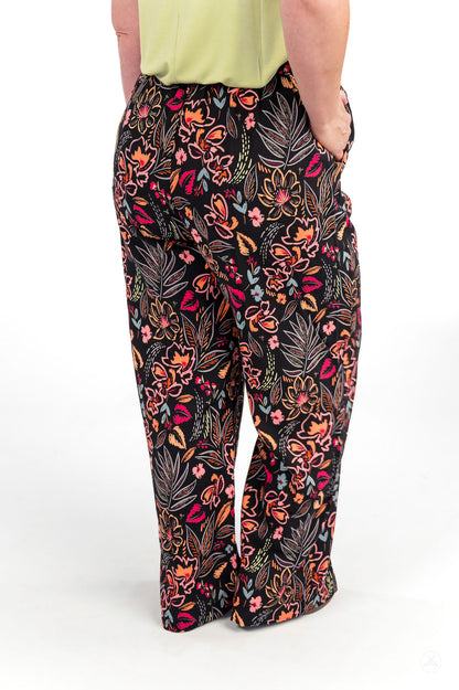 Person standing with hands in pockets wearing floral patterned Breeze Wide-Leg Pant by sweetlegs on white background