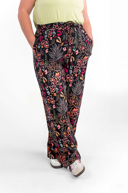 Person wearing black floral patterned Breeze Wide-Leg Pant by sweetlegs with hands in pockets standing against white background