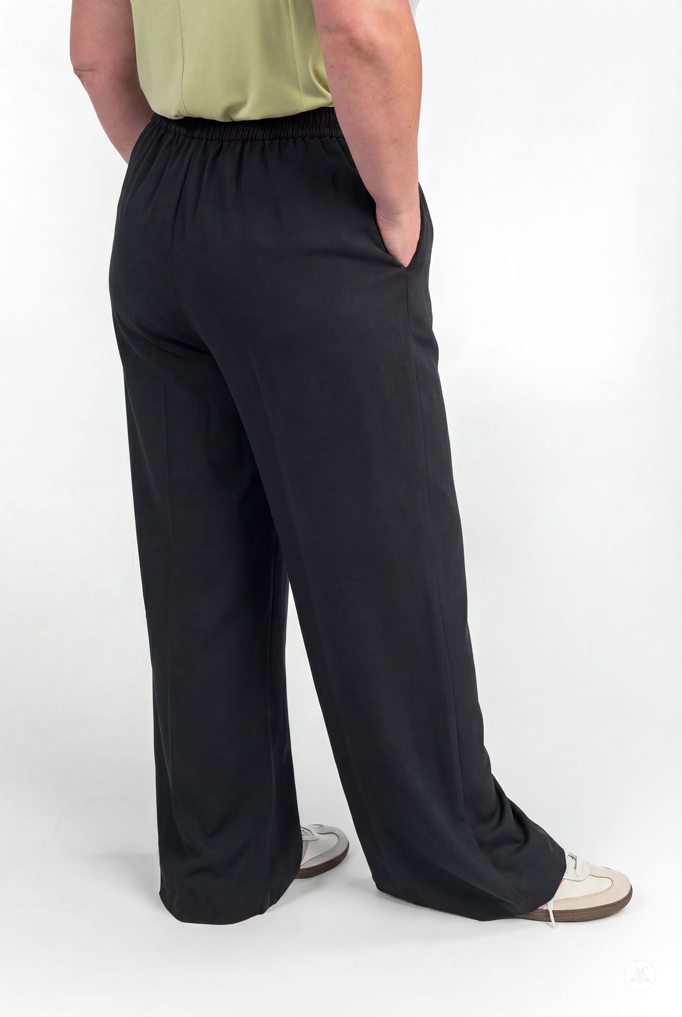 Person standing barefoot wearing black Breeze Wide-Leg Pant by sweetlegs with hands in pockets and light green top visible from back